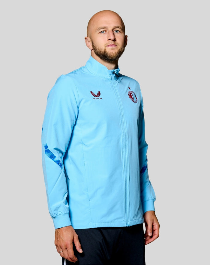 Man wearing a light blue Feyenoord third matchday jacket with full zipper chest logos and dark blue elbow prints