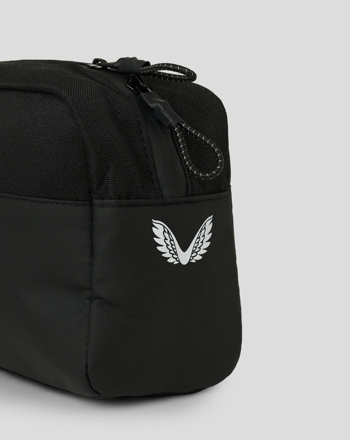 Close up of black Castore Toilettas showing a white wing emblem and braided zipper pull.