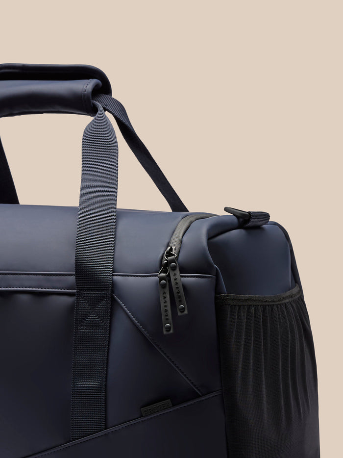 Navy Core Holdall close up showing padded grip, detachable shoulder strap, branded zipper pulls and mesh side pocket