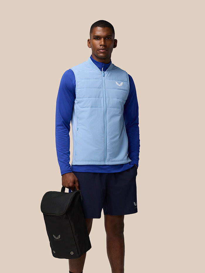 Athlete in blue athletic wear carries a black Castore boot bag during a product shoot.