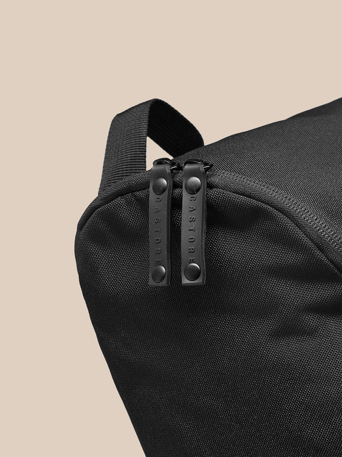 Close up of a black boot bag showing dual zipper pulls embossed with CASTORE on textured fabric