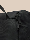 Detail of a black boot bag with zipper pulls and a strap against a beige background