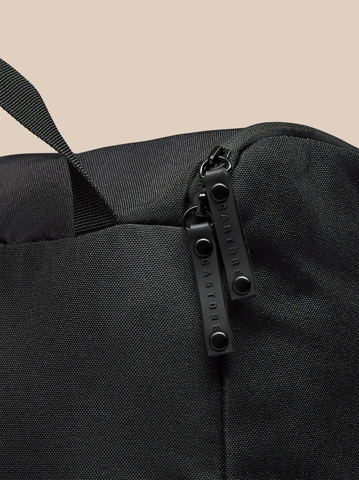 Detail of a black boot bag with zipper pulls and a strap against a beige background