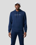 Male model in navy blue ActiveFlex hoodie with front logo and drawstrings, wearing matching pants and a white cap.