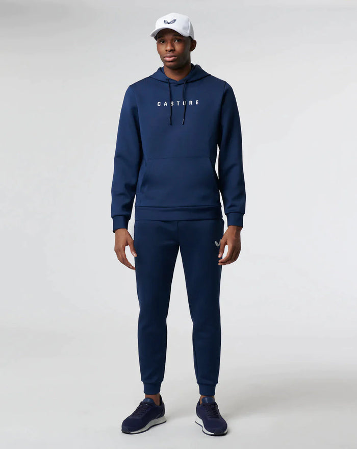 Volledig lichaam van model in donkerblauwe Active Flex hoodie met bijpassende joggers en witte pet.