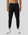Model draagt zwarte Ore Capsule joggingsbroek met trekkoord en subtiele branding, witte sneakers.
