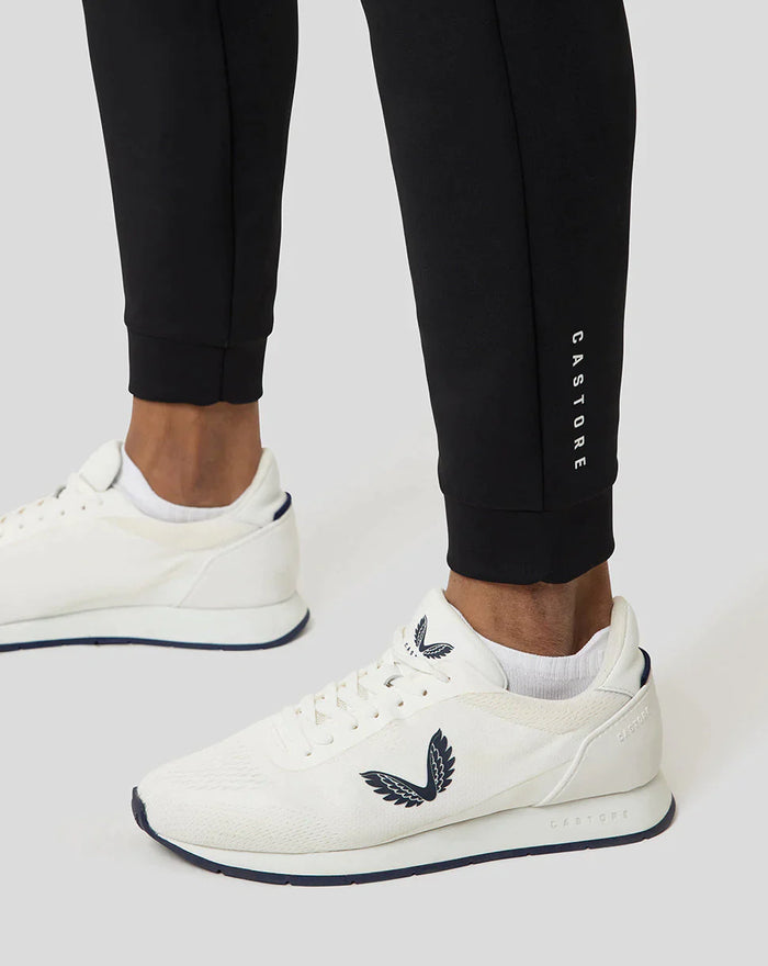 Lower leg view of black Ore Capsule jogging pants with vertical CASTORE branding near the ankle and white sneakers.