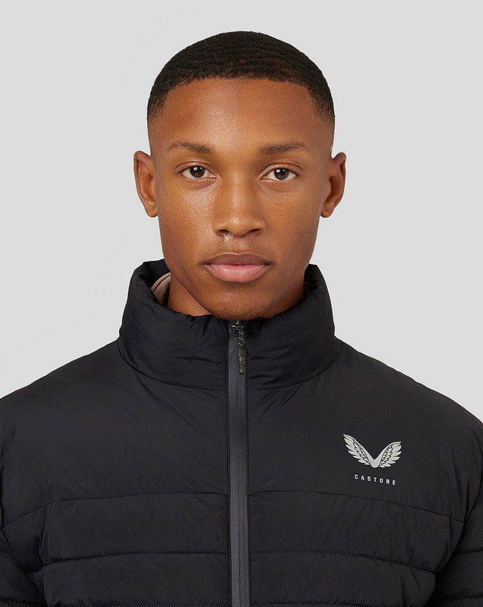 Close up of a man wearing a black Castore lightweight puffer jacket with zip front and chest logo