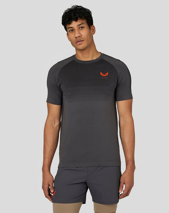 Man draagt donkergrijze Castore Flow trainings T-shirt met gebreid borstpaneel en rode logo.