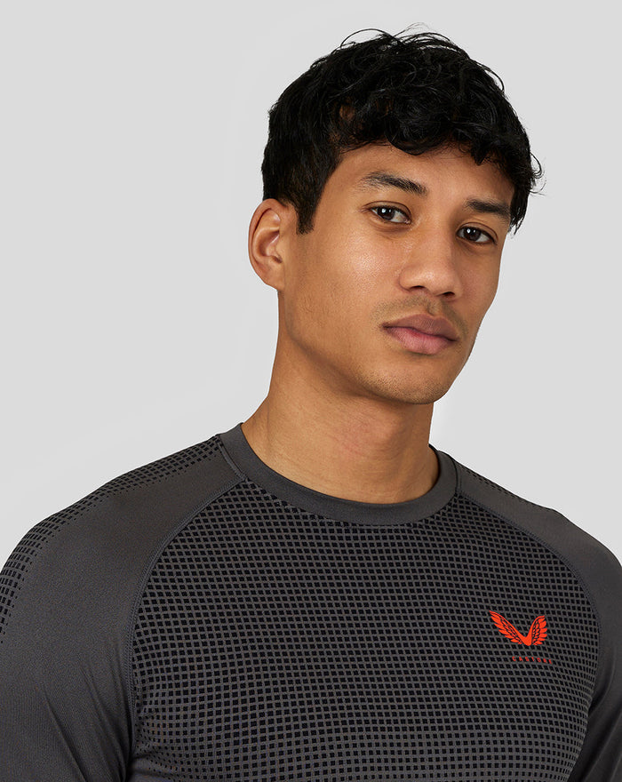 Detail van donkergrijze Castore Flow trainings T-shirt met gebreid borstpaneel en rood logo.