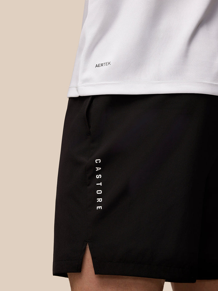 Close-up of white Adapt Graphic T Shirt with Aertek logo on back left hem and black shorts with vertical Castore lettering