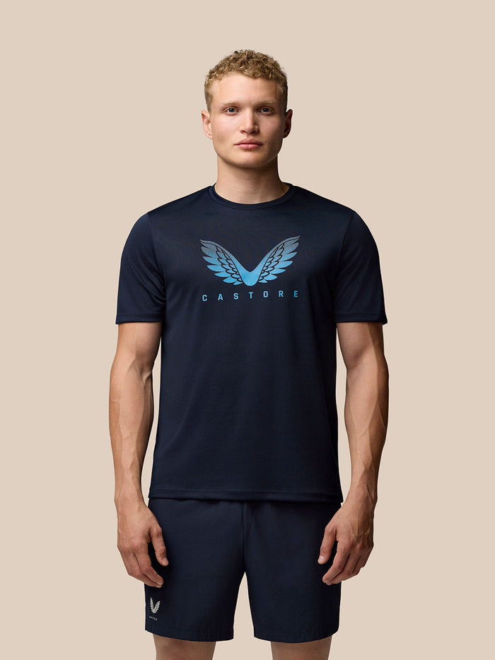 Male model wearing navy graphic T shirt with light blue wing logo on chest