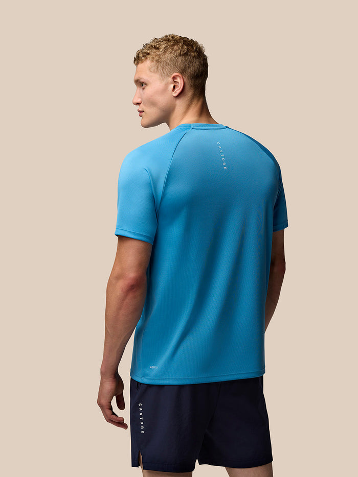 Back view of a male model wearing blue Adapt Short Sleeve T Shirt for men with Castore logo along the back and Aertek logo on the lower back