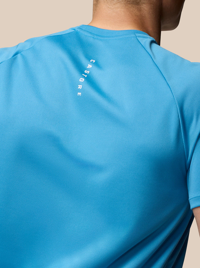 Back view of blue Adapt T Shirt showing vertical CASTORE logo along the spine and Aertek logo on the lower back.