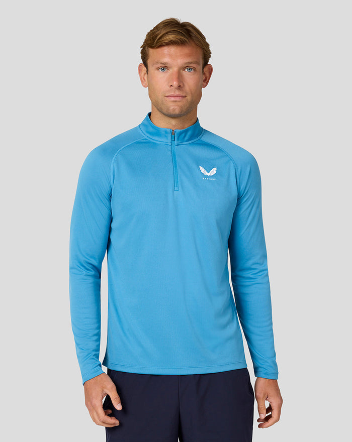 Front view of a man in a light blue quarter zip long sleeve top with Castore logo on chest against a gray backdrop