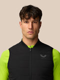 Front view of male model wearing black sleeveless gilet over neon lime sleeves with Castore logo on left chest