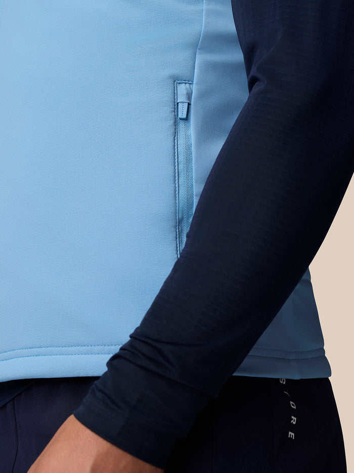 Close-up van lichtblauwe Apex Training Gilet met zijzakken met ritssluiting en reflecterend Castore-logo
