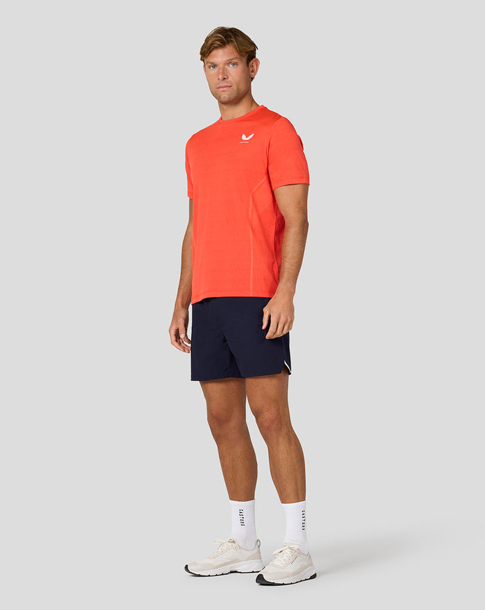 Male model wearing coral Apex Geweven T Shirt Fiesta with navy shorts and white sneakers.