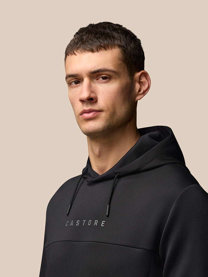 Portrait of a man wearing a black Flex Hoodie with hood and drawstrings against a beige background