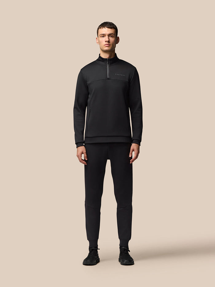 Full-body view of a man in a black Flex Quarter Zip top with matching pants, Castore branding on the chest.
