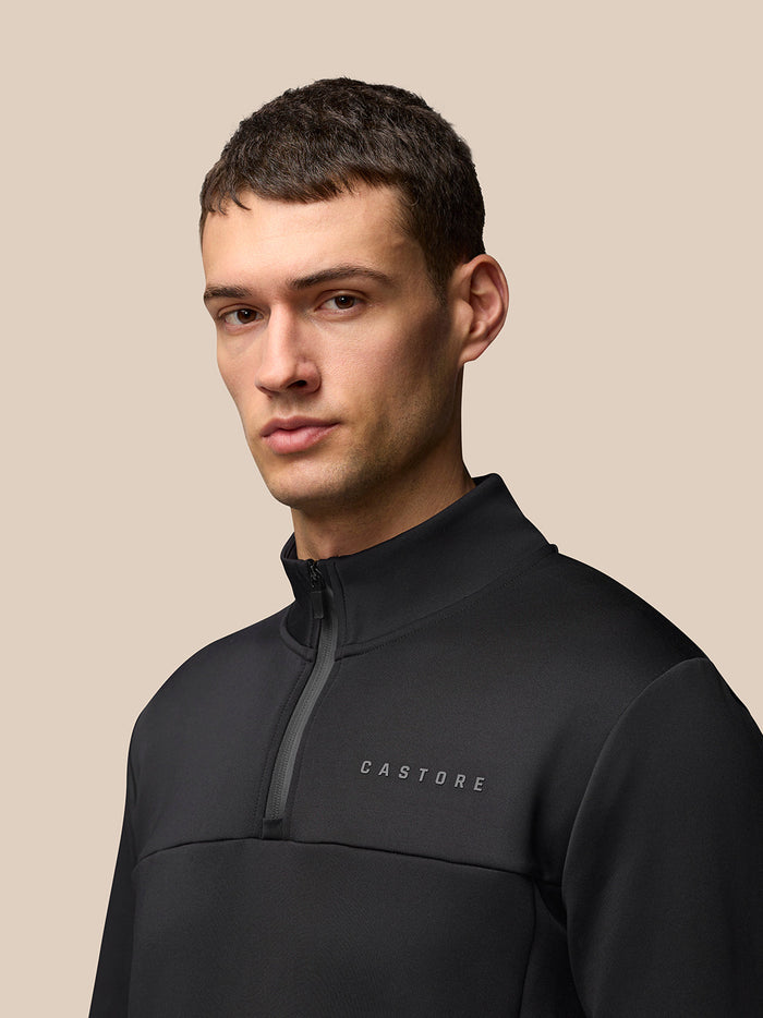 Back view of male model in black Flex Quarter Zip Top with high collar and Protek branding at the hem.