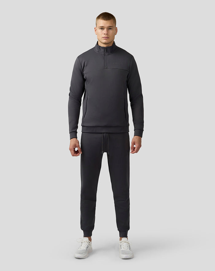Full-body shot of a man in a charcoal Scuba Quarter Zip Top with matching joggers and white sneakers