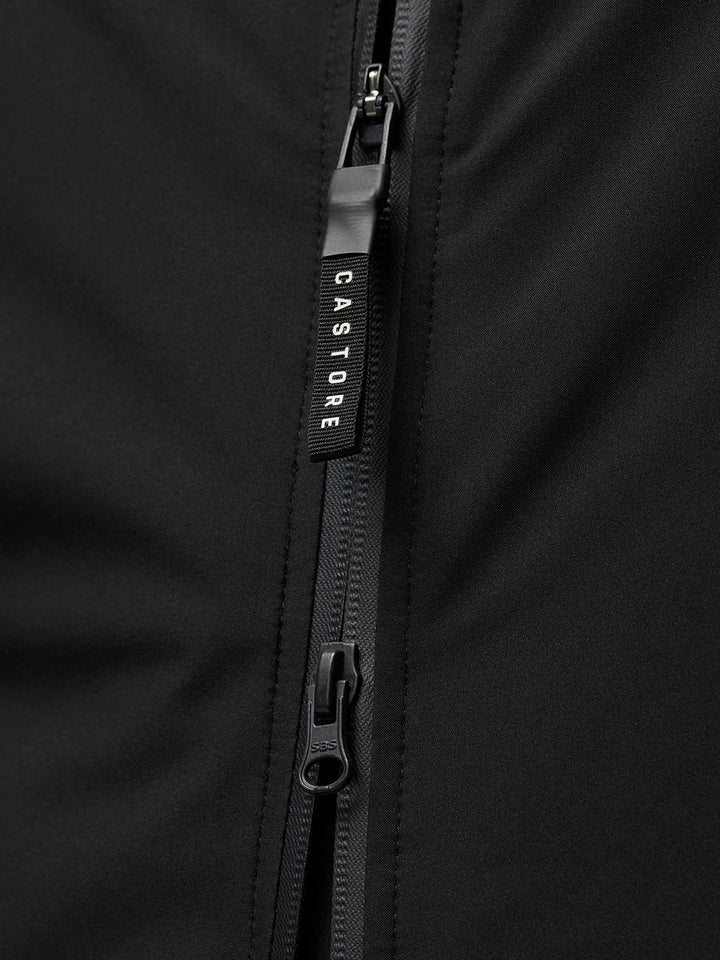 Close-up van een zwarte jas rits met Castore merkpull.