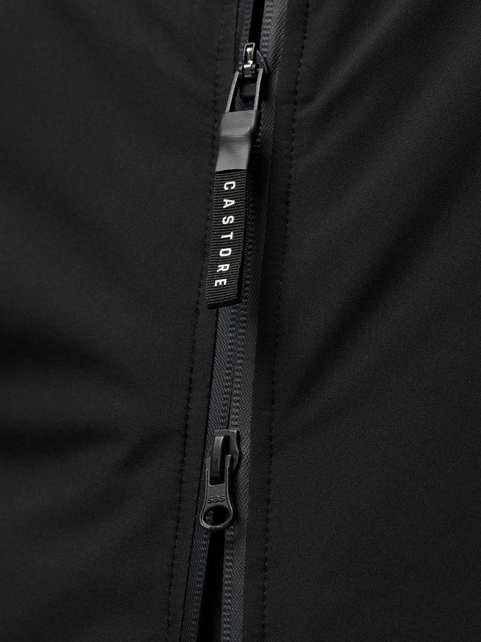 Close-up van een zwarte jas rits met Castore merkpull.