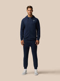 Full body shot of a man in navy Travel Lifestyle Joggers and hoodie set on a beige background