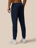Front view of navy Travel Lifestyle Joggers with logo on the thigh and ribbed cuffs paired with white sneakers.