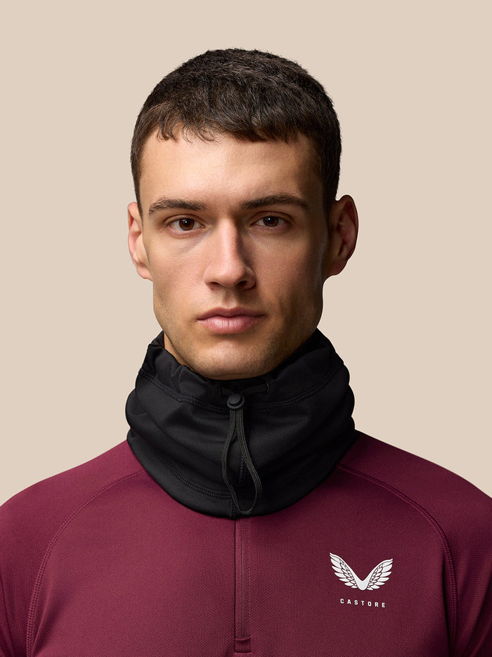 Model draagt zwarte nekwarmer als hoge kraag met trekkoord en Castore branding op kleding