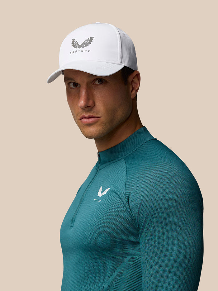 White Castore cap with winged logo on a male model wearing a teal athletic shirt