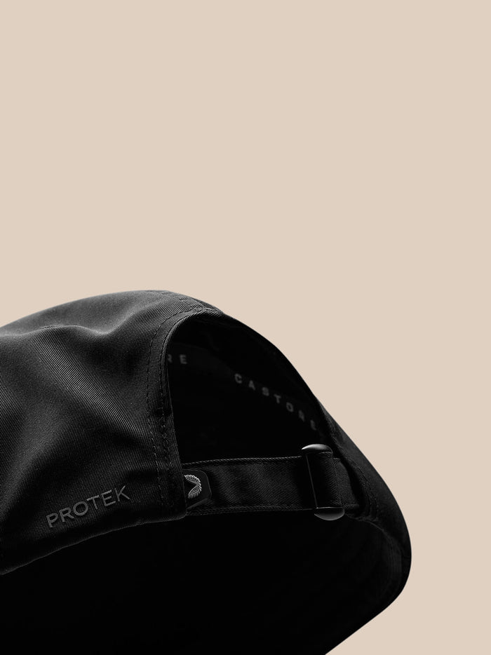 Close up of black Castore Active cap with adjustable strap and Protek branding on a beige background