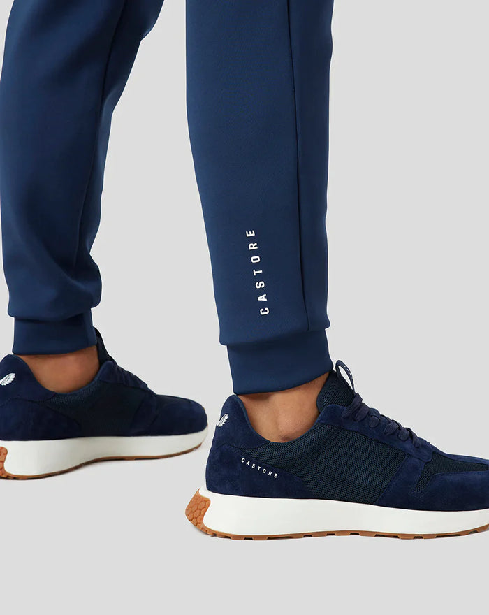 Blue joggers with vertical CASTORE branding along the leg and navy sneakers
