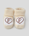 Beige baby booties with white heart patches embroidered with a brown F