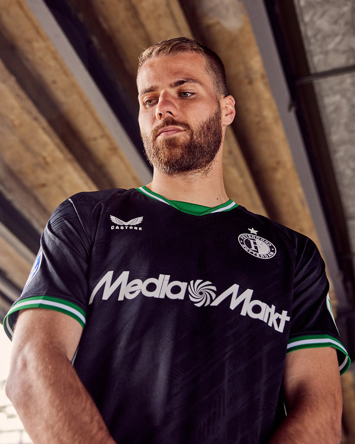 Man wearing black Feyenoord 2024-25 away shirt with green collar and sleeve trim, crest on the left chest and sponsor across the front.