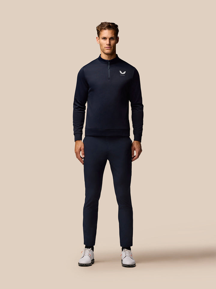Full body shot of male model in navy Golf Club outfit with zip neck top and matching pants, Castore logo on chest.