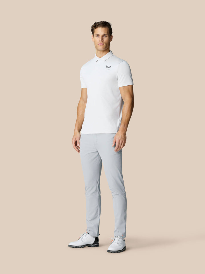 Full-length shot of a man in a white polo and light gray golf pants, standing with a golf club at his side.