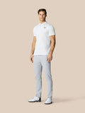 Full-length shot of a man in a white polo and light gray golf pants, standing with a golf club at his side.