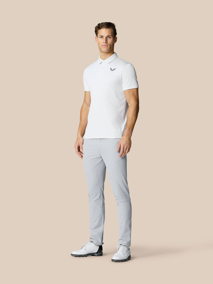 Full-length shot of a man in a white polo and light gray golf pants, standing with a golf club at his side.