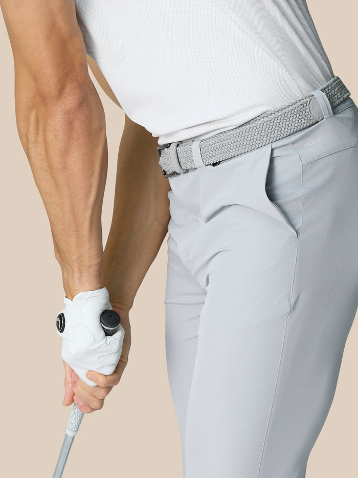 Side view of a man wearing light gray golf pants with a braided belt, holding a golf club.