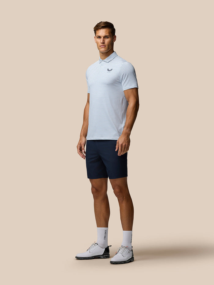Model draagt donkerblauwe Golf Lightweight Shorts en een lichtblauwe gestreepte polo voor een complete golfoutfit