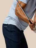 Man met donkerblauwe golfshorts en een wit met blauwe strepen polo houdt een golfclub vast