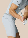 Profile view of a man in light gray golf shorts with belt showing Castore logo on right thigh