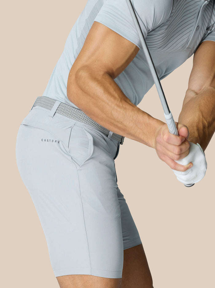 Profile view of a man in light gray golf shorts with belt showing Castore logo on right thigh
