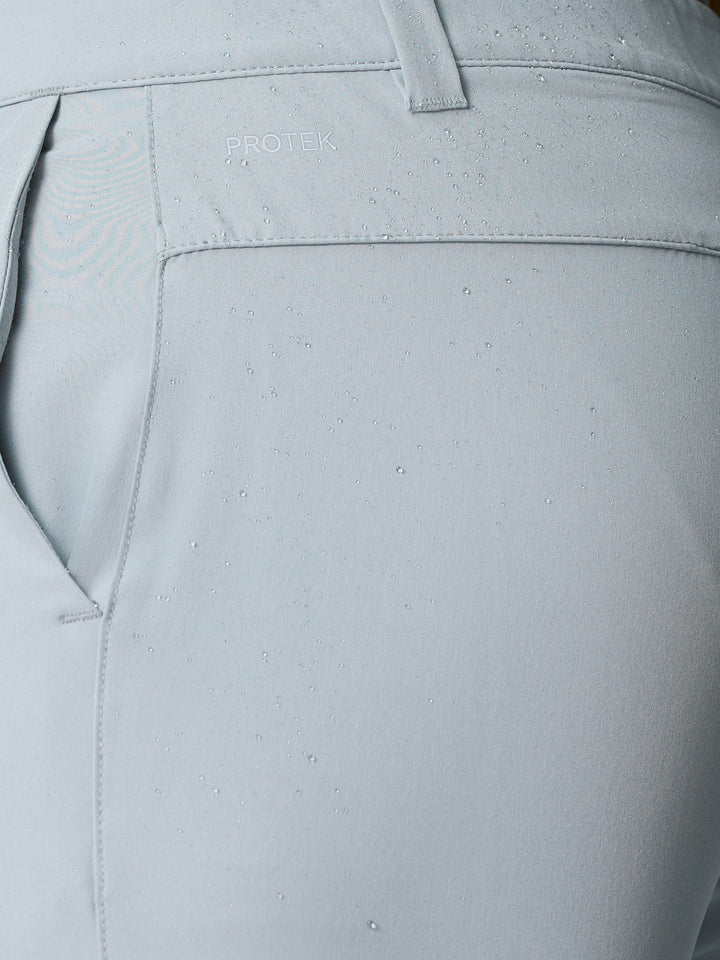 Close-up of light gray golf shorts fabric with water droplets and ProTek logo