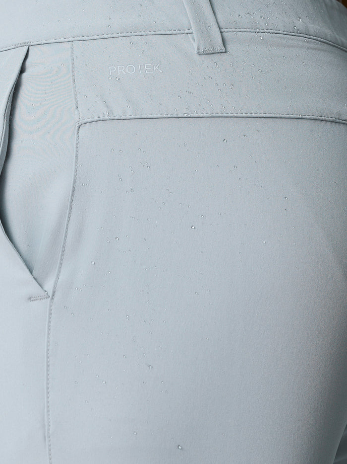 Close-up of light gray golf shorts fabric with water droplets and ProTek logo