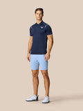 Male model in navy polo and light blue golf shorts on a beige background