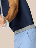 Back view of golfer in navy shirt and light blue shorts with braided belt and visible Castore logo and ProTek branding on the back pocket
