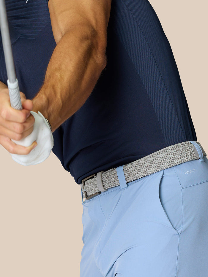 Back view of golfer in navy shirt and light blue shorts with braided belt and visible Castore logo and ProTek branding on the back pocket